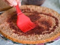 A woman applying cherry syrup on to a half of a homemade gluten free sponge cake with a cooking brush