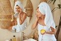 Woman Applying Clay Mask. Wrapped In Bath Towel Model Looking At Mirror And Using Skin Care Product For Derma.