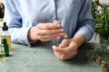 Woman applying essential oil on wrist at wooden table,