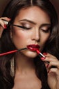 Woman applying Make up. Beauty Model Girl put on Red Lipstick. Professional Makeup Artist painting Lips, holding Mascara and Eye Royalty Free Stock Photo