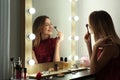 Woman applying makeup near mirror with light bulbs Royalty Free Stock Photo