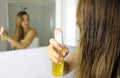 Woman applying oil mask spray on hair in front of a mirror. Hair care concept. Focus on hair
