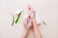 Woman applying organic cream on hands, aloe vera leaves and cream container on light beige surface. Top view Royalty Free Stock Photo