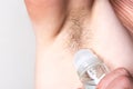 Woman is applying roll on antiperspirant to her armpit with hair on grey background.