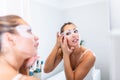 Woman is applying sheet mask on her face in the bathroom. Skin care girl touch patches of fabric mask under eyes to reduce eye Royalty Free Stock Photo