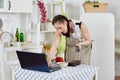 Woman with notebook and phone cooks in kitchen. Isolation period, quarantine, social distancing. Remote education or remote work Royalty Free Stock Photo