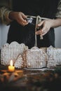 Woman in apron sprinkling sugar powder on christmas gingerbread houses on rustic wooden table. Atmospheric moody image. Christmas