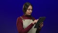Woman in apron using tablet over isolated blue background suggests a young waitress engaged in work with technology in a modern Royalty Free Stock Photo