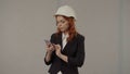 A woman architect takes notes in a smartphone. Business woman in a protective helmet and with a smartphone on a gray