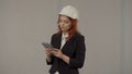 A woman architect takes notes in the tablet. Business woman in a protective helmet and with a tablet on a gray