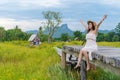 Woman with arm raised on wooden bridge with yellow cosmos flower field
