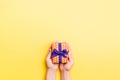 Woman arms holding gift box with colored ribbon on yellow table background, top view and copy space for you design Royalty Free Stock Photo