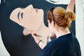 Woman artist draws with paint brush surreal girl portrait on white canvas at art painting