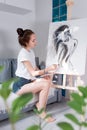 Woman artist, draws a silhouette of a girl with long hair on a white background, at home in workshop, in her hand a Royalty Free Stock Photo