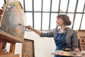 Woman artist paints a picture on canvas. Bright art studio with a large window. Easels and canvases. Royalty Free Stock Photo