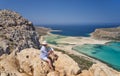 Woman artist sits on the stones and paints a picture of Tigani cape and Balos lagoon with sandy beach. Crete, Greece Royalty Free Stock Photo