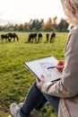 Woman artist sketching portrait of horse on pasture