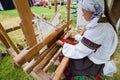 Woman artist in Ukrainian traditional clothes works at ancient loom, weaving carpet