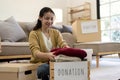 Woman asian holding donation box full with clothes and select clothes. Concept of donation and clothes recycling