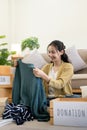 Woman asian holding donation box full with clothes and select clothes. Concept of donation and clothes recycling