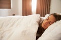 Woman Asleep In Bed As Sunlight Comes Through Curtains Royalty Free Stock Photo