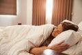 Woman Asleep In Bed As Sunlight Comes Through Curtains