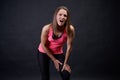 Woman athlete runner stands on an isolated black background in a pink tank top and holds knee and thigh from severe burning pain Royalty Free Stock Photo