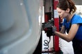 Woman auto mechanic removes a car wheel on car lift