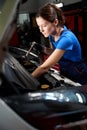Woman auto mechanic works under an open hood