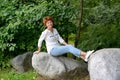 The woman of average years sits on a boulder in the park