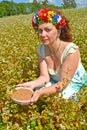 The woman of average years with a wreath on the head holds a bowl with buckwheat in the field of the blossoming buckwheat