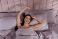 Woman awakening in comfortable bed with light grey striped linens, above view