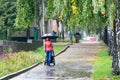 A woman with a baby carriage walks down the street in the rain with an umbrella. Rear view