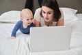 Woman with baby lying at home in bed looking with interest at laptop Royalty Free Stock Photo