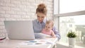 Woman with baby not concentrated at work. Business mother looking documents