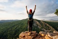 A woman with a backpack standing against the background of mountains with her hands raised, rear view. Royalty Free Stock Photo