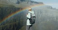 Woman with backpack standing at cliff edge looking at rainbow over the canyon in Iceland Royalty Free Stock Photo