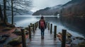 a woman with a backpack standing on a wooden bridge over a lake Royalty Free Stock Photo