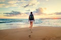 Woman with backpack walk on the ocean sand beach at sunset time Royalty Free Stock Photo