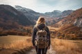 A woman with a backpack walks along the path in the mountains. A female hiker walking to mountains rear view, AI Generated Royalty Free Stock Photo