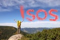 Woman with backpack and word SOS made of color smoke bomb on rocky peak in mountains Royalty Free Stock Photo