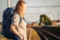 Woman backpacker checks on smartphone train delay at railway station Royalty Free Stock Photo