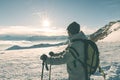 Woman backpacker with hiking poles looking at view high up on the Alps. Rear view, winter cold snow, sun star in backlight, split
