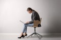 Woman with bad posture using laptop while sitting on chair near light grey wall indoors Royalty Free Stock Photo