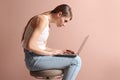 Woman with bad posture using laptop while sitting on stool against pale pink background Royalty Free Stock Photo