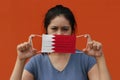 A woman with Bahrain flag on hygienic mask in her hand and lifted up the front face on orange color background. Tiny Particle or