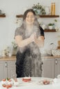 Woman baker clapping and sprinkling white flour over dough on kitchen background Royalty Free Stock Photo