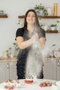 Woman baker clapping and sprinkling white flour over dough on kitchen background Royalty Free Stock Photo