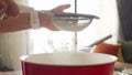 Woman baker sifting flour for dough through bolter.