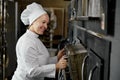 Woman baker in uniform opening oven stove at bakery kitchen Royalty Free Stock Photo